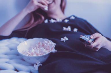 Woman watching tv and eating popcorn